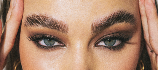 Close-up of thick, well-groomed eyebrows with light-colored eyes, long lashes, and smokey eye makeup.